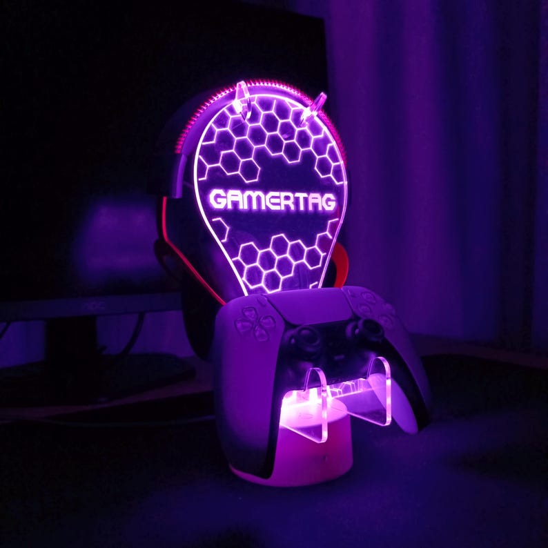 May include: A purple and white LED light stand with a honeycomb design and the word "GAMERTAG" printed on it. The stand is designed to hold a video game controller.