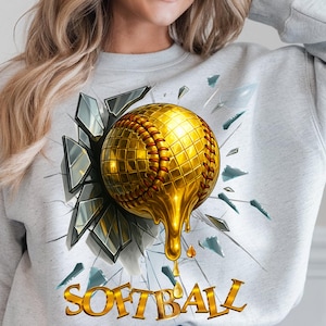 May include: A grey sweatshirt with a graphic of a gold softball breaking through a cracked glass window. The text "SOFTBALL" is printed below the graphic.