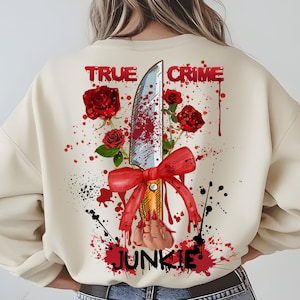 May include: A cream colored sweatshirt with a graphic print of a bloody knife tied with a red bow and red roses. The text "TRUE CRIME JUNKIE" is printed on the sweatshirt.