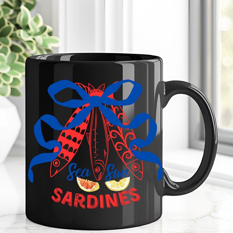 Puede incluir: Taza de caf&eacute; de cer&aacute;mica negra con una cinta azul y tres peces rojos y blancos con el texto "Sea Sun Sardines" en rojo y blanco.