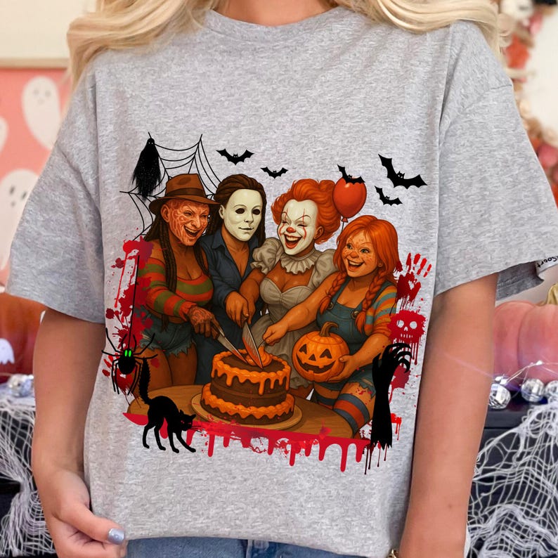 K&ouml;nnte beinhalten: Graues T-Shirt mit einem Halloween-Motiv. Das Design zeigt vier Horrorfilm-Charaktere um einen Kuchen, mit Flederm&auml;usen, einem Spinnennetz und einer schwarzen Katze. Das Bild hat einen Cartoon-Stil mit roten Akzenten.