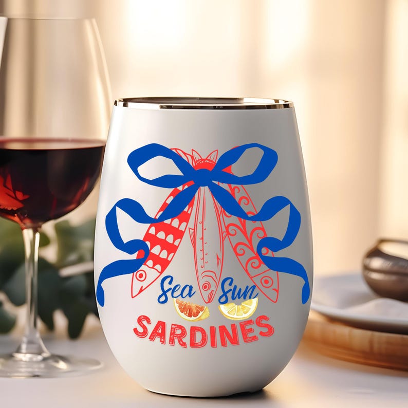 Puede incluir: Vaso de vino blanco sin tallo con una cinta azul y una ilustraci&oacute;n roja y blanca de sardinas con el texto "Sea Sun Sardines".