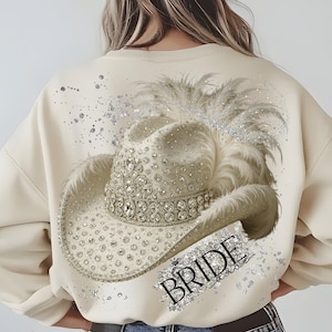 May include: A cream-colored sweatshirt with a rhinestone-encrusted cowboy hat and the word "BRIDE" in sparkly silver lettering.