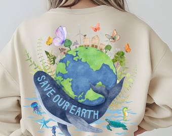 May include: A beige sweatshirt featuring a watercolour illustration of a whale holding the Earth. The Earth is surrounded by butterflies, trees, and buildings. The text "SAVE OUR EARTH" is written on the whale's body.