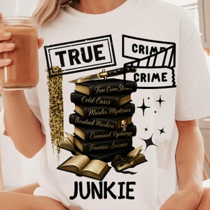 Könnte beinhalten: Weißes T-Shirt mit einem Grafikdesign, das einen Stapel schwarzer Bücher mit goldfarbenen Buchstaben, ein Messer und die Worte "TRUE CRIME JUNKIE" zeigt. Die Bücher tragen Titel wie "Cold Cases" und "Murder Mysteries".