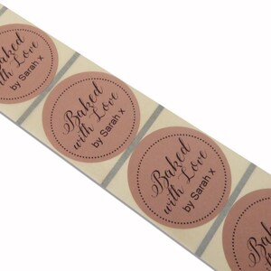 May include: A roll of round, brown, paper stickers with the text "Baked with Love by Sarah x" in black cursive font.