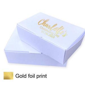 Puede incluir: Dos cajas de regalo blancas con una impresión en lámina dorada que dice "Charlotte's Christening Day 01.05.2023".