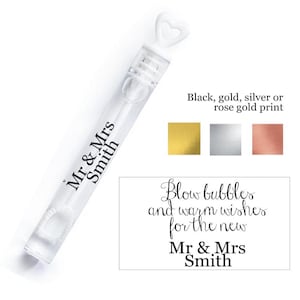 Può includere: Una bacchetta per bolle di sapone in plastica bianca con un manico a forma di cuore. La bacchetta è etichettata "Mr & Mrs Smith". Il testo "Blow bubbles and warm wishes for the new Mr & Mrs Smith" è stampato su un cartoncino bianco. Il testo "Black, gold, silver or rose gold print" è stampato sopra quattro piccoli quadrati che mostrano i diversi colori di stampa.