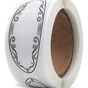 May include: A roll of white stickers with a black decorative border. The border has an ornate design with curved lines and swirls. The stickers are blank in the center, ready for custom printing or labeling.