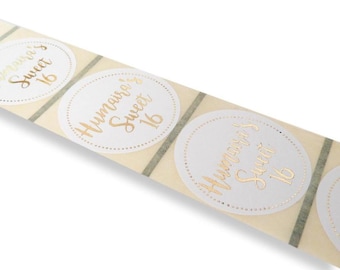 Könnte beinhalten: Rolle mit weißen runden Aufklebern mit goldener Schrift "Hummaira's Sweet 16".