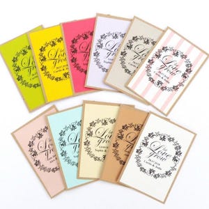 May include: A collection of ten seed packets with a brown kraft paper background and a variety of coloured paper inserts. Each packet features a black and white design of a floral wreath with the text "Let Love Grow" and a wedding date.