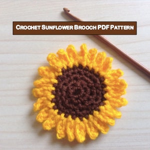 May include: A crocheted sunflower brooch in yellow and brown. The brooch is made with a crochet hook and yarn. CROCHET SUNFLOWER BROOCH PDF PATTERN.