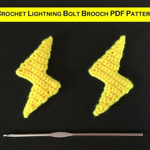 May include: Two yellow crocheted lightning bolt brooches. The brooches are made with a yellow yarn and are about 3 inches tall. The brooches are on a black background. The image also shows a crochet hook.