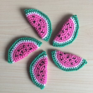 May include: Five crocheted watermelon slices in shades of pink, green, and white. Each slice has a black seed pattern.