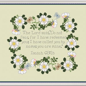 May include: A cross-stitch pattern featuring a floral wreath of white roses with green leaves and a verse from the Bible: "The Lord said, 'Do not fear, for I have redeemed you; I have called you by name; you are mine.' Isaiah 43:16"