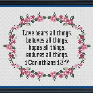 以下が含まれることがあります： 黒い文字でLove bears all things, believes all things, hopes all things, endures all things. 1 Corinthians 13:7と刺繍され、ピンクと赤の花と緑の葉の装飾的な楕円形のリースで囲まれた、額縁入りのクロスステッチ刺繍。