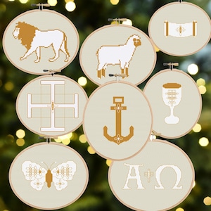 May include: Eight cross-stitch embroidery hoops with religious motifs. Designs include a lion, lamb, cross, anchor, chalice, butterfly, scroll, and the Greek letters Alpha and Omega. The colour scheme is beige, white, and gold.