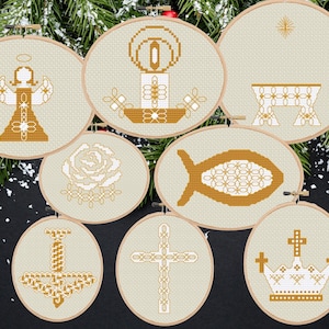 May include: Seven embroidered Christmas ornaments in wooden hoops. Each features a different religious symbol: an angel, a candle, a manger, a rose, a fish, a chalice, a cross, and a crown. The ornaments are in beige and gold, set against a festive backdrop.