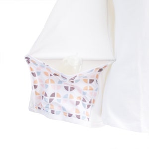 Puede incluir: Camiseta blanca de manga larga con un bolsillo oculto que tiene un patr&oacute;n geom&eacute;trico en tonos de rosa, marr&oacute;n y azul. El bolsillo est&aacute; dise&ntilde;ado para guardar una botella peque&ntilde;a u otros art&iacute;culos.