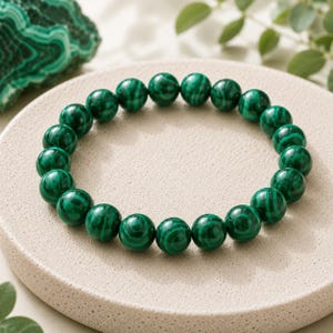 Peut inclure: Un bracelet circulaire composé de perles de malachite sphériques et polies. Chaque perle présente un motif naturel distinct avec des bandes alternant des nuances de vert forêt profond et de noir, assemblées en une boucle continue et souple.
