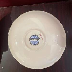 May include: White saucer with a blue and white logo that reads "colclough" and "Bone China Made in England 8008".
