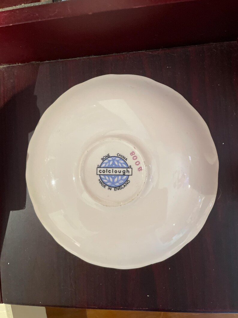 May include: White saucer with a blue and white logo that reads "colclough" and "Bone China Made in England 8008".