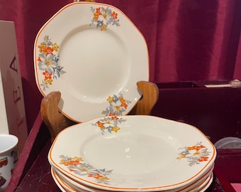 May include: A stack of five white ceramic plates with a floral design in shades of orange, yellow, and blue. The plates have a scalloped edge and a raised rim.