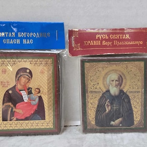 May include: Two framed religious icons. The first icon features a depiction of the Virgin Mary holding a baby Jesus. The text on the frame reads "Пресвятая Богородица, спаси нас". The second icon features a bearded man in a robe. The text on the frame reads "Русь святая, храни веру православную".