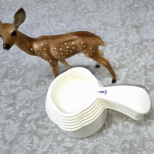 May include: A set of white plastic measuring cups, stacked together. The top cup has a blue label that reads "1/4 Cup".