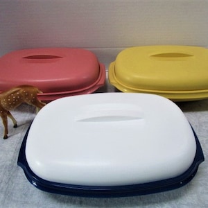 May include: Three oval-shaped serving dishes with lids. The dishes are pink, yellow, and white with blue trim. The lids have a slight indentation in the center.