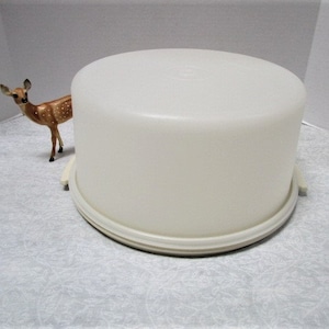 May include: White plastic cake stand with a smooth, rounded top and a slightly raised edge. The stand has a white plastic base with a smooth, flat surface.