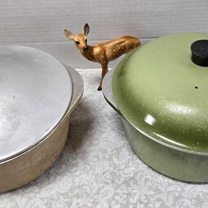 May include: Two vintage enamel Dutch ovens with lids. One is silver with a black knob and the other is green with a black knob.