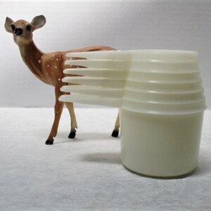 May include: A set of white plastic measuring cups stacked on top of each other. The cups are nested together and have a smooth, white finish.
