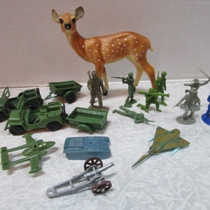 May include: A collection of vintage toy soldiers, vehicles, and a deer figurine. The set includes green jeeps, a plane, a cannon, and various soldier figures in green, gray, and blue. The deer is brown with white spots.