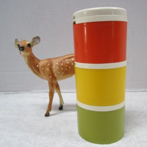May include: A three-tiered container with a white lid. The container is red, yellow, and green. The container is sitting on a white surface.