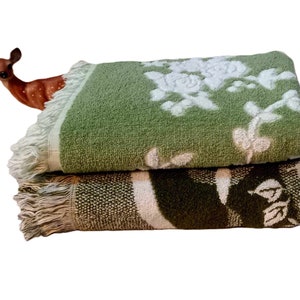 May include: Two green and brown bath towels with white floral designs and fringed edges. The towels are stacked on top of each other.