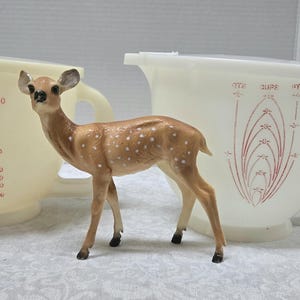May include: Two off-white vintage mixing bowls with red measurement markings and handles. A small, brown and white spotted deer figurine stands in front of the bowls. The bowls have a capacity of up to 1500 units.