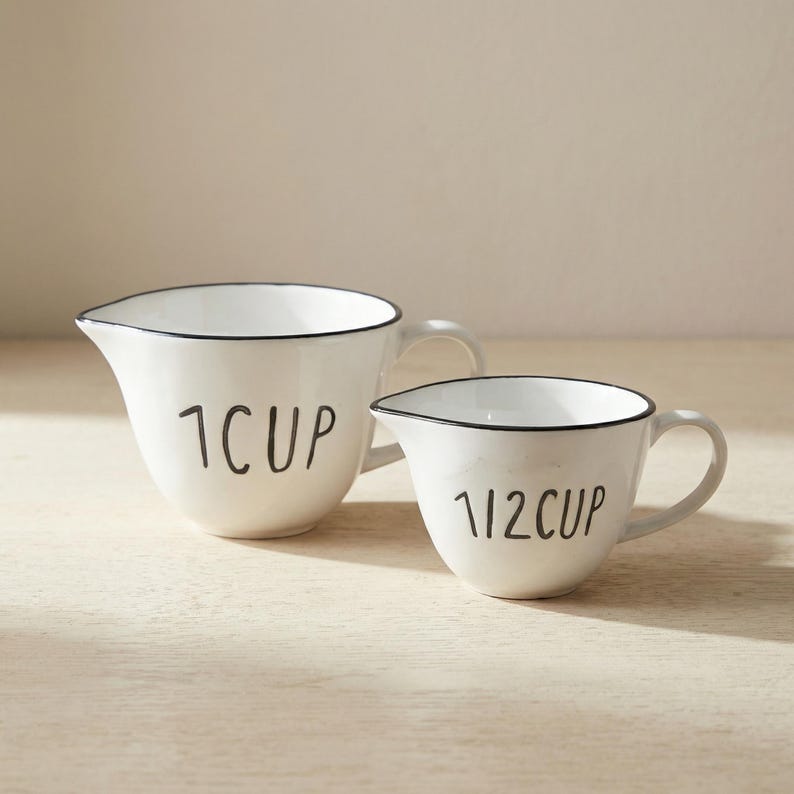 May include: A white ceramic mug with a black handle and the text "But First, Coffee" in a black, bold font. The mug is on a wooden surface. The mug is approximately 10 cm tall.