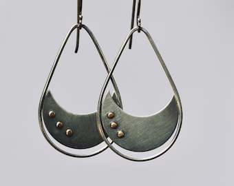 May include: A pair of silver teardrop-shaped earrings with a crescent moon shape and gold accents.