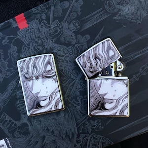 May include: Two rectangular metal lighters with a polished silver finish. Each lighter features a detailed black and white ink-style illustration of a person with long wavy hair and delicate facial features printed on the front surface.