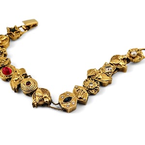 May include: A gold charm bracelet with a variety of charms, including stars, flowers, and geometric shapes. The charms are adorned with colorful gemstones, including red, blue, and white.