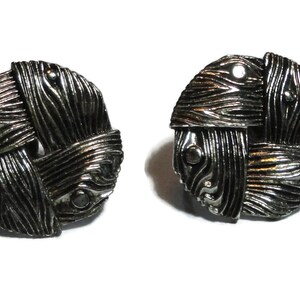 May include: A pair of silver tone earrings with a woven design. The earrings are round and have a textured surface.