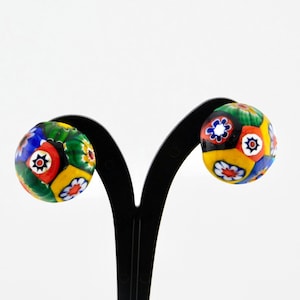 May include: A pair of colorful glass earrings with a floral pattern. The earrings are round and have a multi-colored design with shades of red, yellow, green, blue, and black.