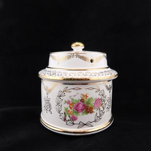 May include: White ceramic jar with a gold lid and floral design. The jar has a gold trim and a floral pattern with pink, orange, and yellow flowers.