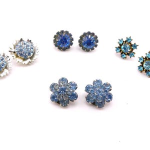 May include: A collection of vintage earrings in various styles, all featuring blue gemstones. Styles include flower-shaped, round, and cluster designs. The earrings are set in silver and gold-toned metal, with a bright white background.