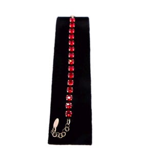 May include: A delicate bracelet featuring a row of vibrant red gemstones set in a silver-toned metal. The gemstones are square-cut and evenly spaced, creating a continuous line of color. The bracelet is displayed on a black surface.