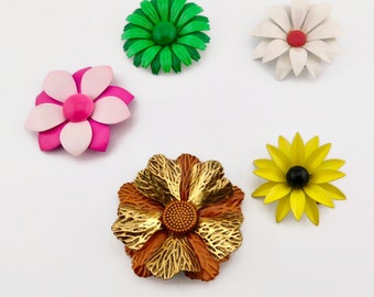 May include: Five vintage flower brooches in various colors and styles. The brooches are made of metal and have a shiny finish. The flowers are in shades of green, white, pink, yellow, and orange.