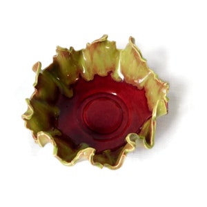 May include: A ceramic bowl with a red interior and a green exterior. The bowl has a ruffled edge and a glossy finish.