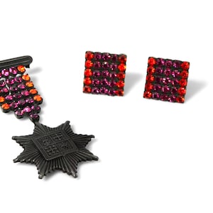 May include: A set of earrings and a brooch featuring a black metal design with red and pink rhinestones. The earrings are square shaped and the brooch is a star with a smaller square in the center.