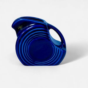 May include: A cobalt blue ceramic pitcher with a circular design. The pitcher has a handle and a spout for pouring. The design features concentric circles that create a textured appearance. The pitcher is a decorative item.
